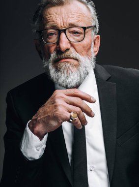 Siyah takım elbiseli olgun sakallı aktör çenesinin altında elle düşünüyor.