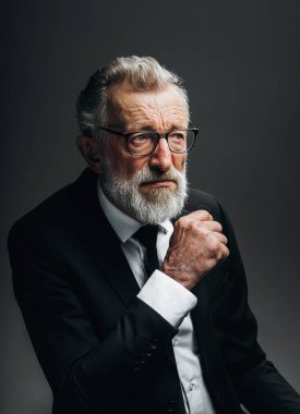 Resmi siyah takım elbiseli dalgın bir iş adamı, avuçlarını çenesinin yanında tutuyor..