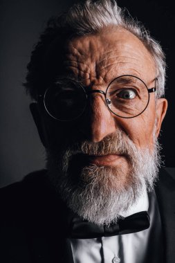 Takım elbiseli, papyonlu yaşlı adamın yüzü kameraya deli gibi bakıyor.