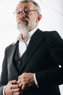 Yuvarlak gözlüklü, şık takım elbiseli, kameraya bakan olgun, akıllı bir adam.