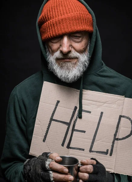 Desempleado viejo mendigo sosteniendo un letrero escrito a mano para ayuda y una taza para monedas — Foto de Stock