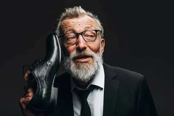 Positive old man in suit, holding near head shoes as handle of vintage phone