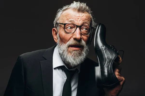Θετικός γέρος με κοστούμι, κρατώντας κοντά στο κεφάλι παπούτσια ως λαβή της vintage τηλέφωνο — Φωτογραφία Αρχείου