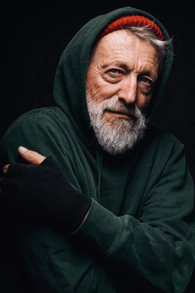 Homeless man dressed in green old clothing shivers from cold, tries to warm up. — Stock Photo, Image