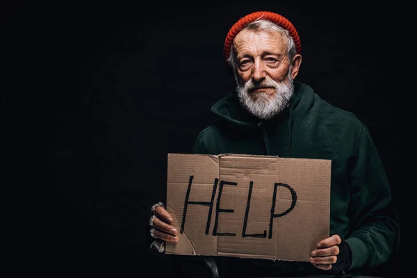 Sad exhausted old-aged bum in red hat and street wear holding a cardboard sign. — Stock Photo, Image