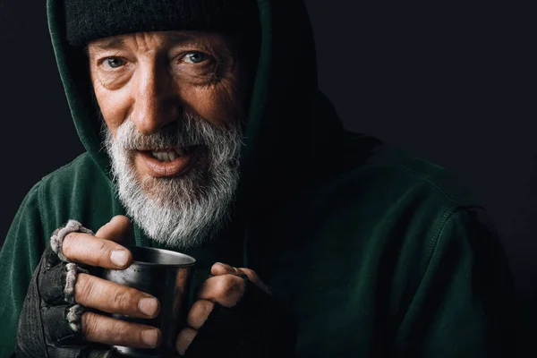 Frozen homeless old man with wrinkled face holds a cup with coins given as alms — Stock Photo, Image