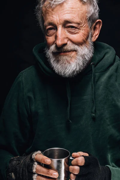 一个满脸皱纹的冻僵的无家可归的老人手里拿着一个杯子，里面装着作为施舍的硬币 — 图库照片