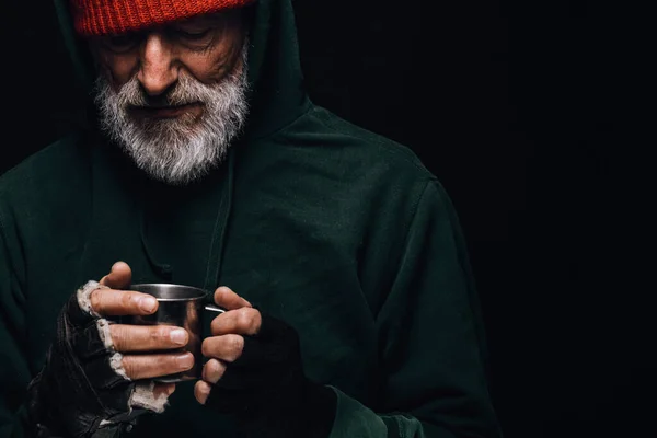 Vieil homme sans abri à la barbe grise tenant une tasse de thé chaud pour se réchauffer. — Photo