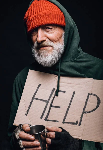 Desempleado viejo mendigo sosteniendo un letrero escrito a mano para ayuda y una taza para monedas — Foto de Stock
