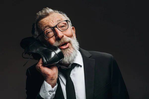 Positieve oude man in pak, houden in de buurt van hoofd schoenen als handvat van vintage telefoon — Stockfoto