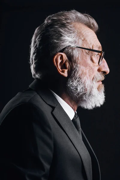 Profile of handsome elderly CEO posing in black formal suit on dark background
