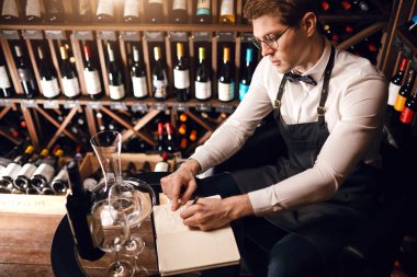 Erkek mağara adamı şişeleri şarapla inceleyip not defterine not alıyor.