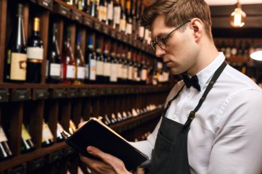 Erkek mağara adamı şişeleri şarapla inceleyip not defterine not alıyor.