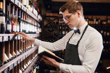Sommelier şarap dükkanındaki şarap ürünleri hakkında bilgi yazıyor.