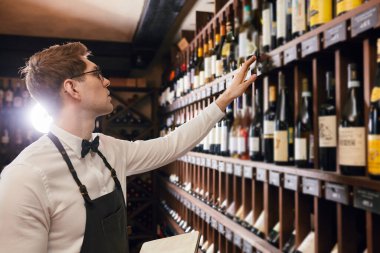 Profesyonel bir mağara adamı şarap raflarının yanında duran degustrasyon kartına notlar yazıyor.