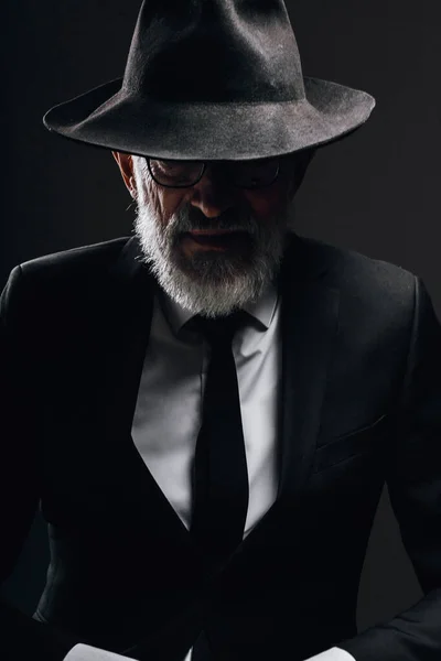 Чоловік похилого віку, зображаючи англійського таємного агента з капелюхом на очах проти темної стіни. — стокове фото