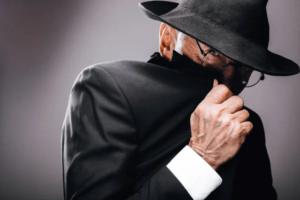 Een oude mannelijke acteur spelen een Engels spion rol, verbergen achter fedora hoed. — Stockfoto