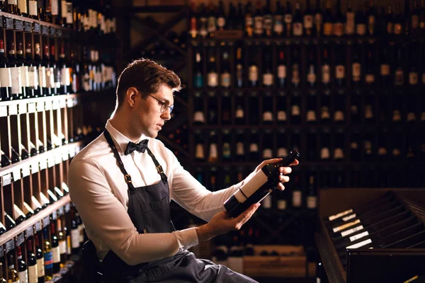 Елегантний продавець вина тримає пляшку вина і читає ярлик у винному магазині — стокове фото