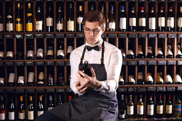 Elegant wine seller holding a bottle of wine and reading label in a wine store