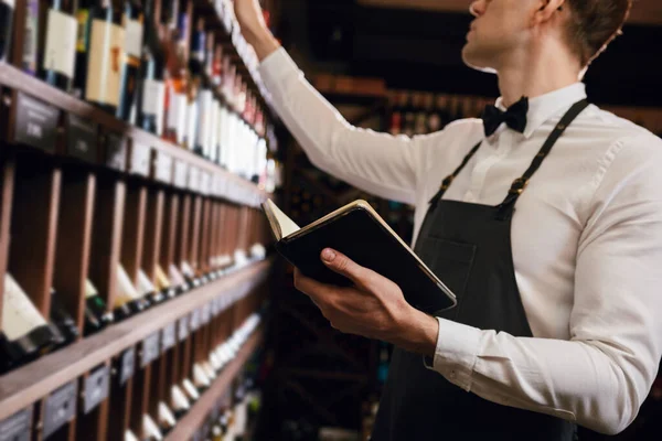 Erkek mağara adamı şişeleri şarapla inceleyip not defterine not alıyor.