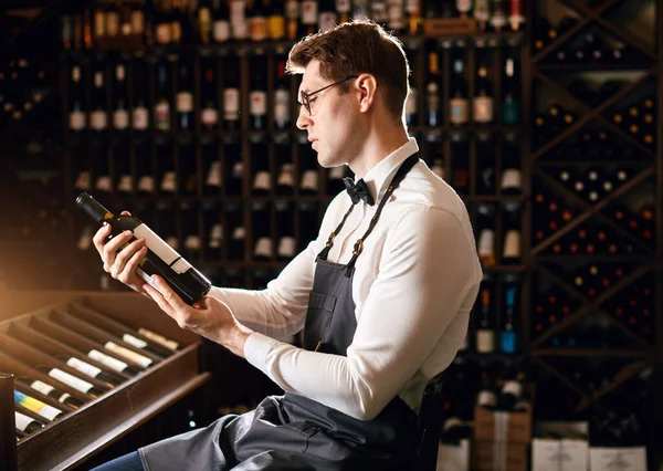 Elegant wine seller holding a bottle of wine and reading label in a wine store