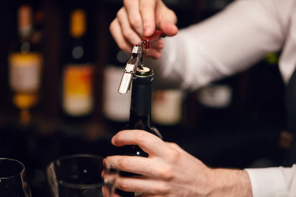 Barista aprire una bottiglia di vino con cavatappi nel ristorante con mensole per vino. — Foto Stock