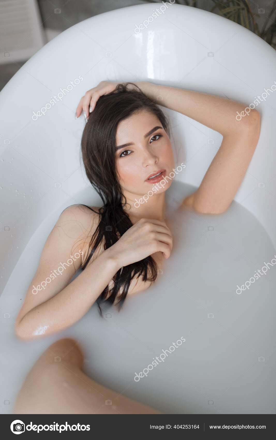 Attractive girl with open eyes takes a milk bath, touching her face