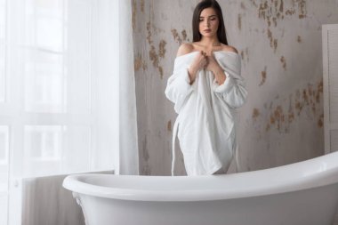 Beyaz cüppeli Spa Avrupalı kız, banyoya hazırlanıyor, suya bakıyor.