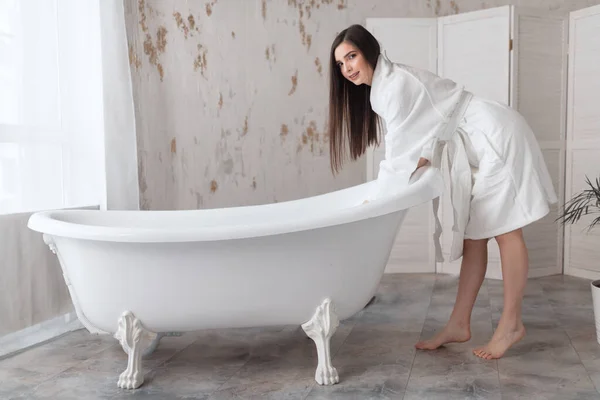 Mujer de cabello castaño en albornoz, posando con hombros desnudos junto al tubo de baño — Foto de Stock