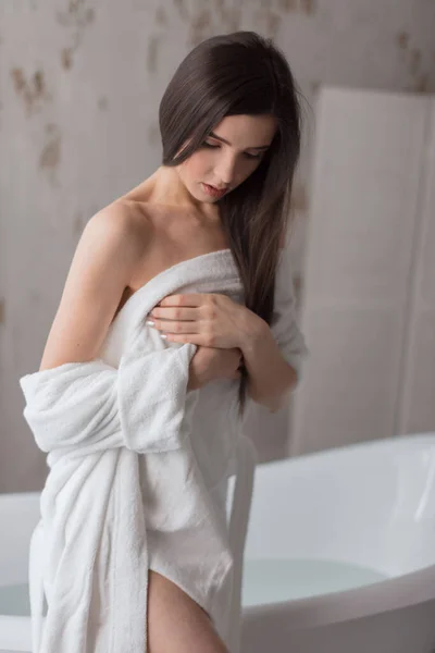 Jeune femme en peignoir blanc assis sur le côté du bain blanc autoportant — Photo