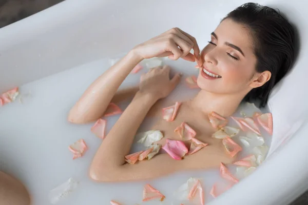 Mujer joven toma un baño de aroma de leche con pétalos de flores — Foto de Stock