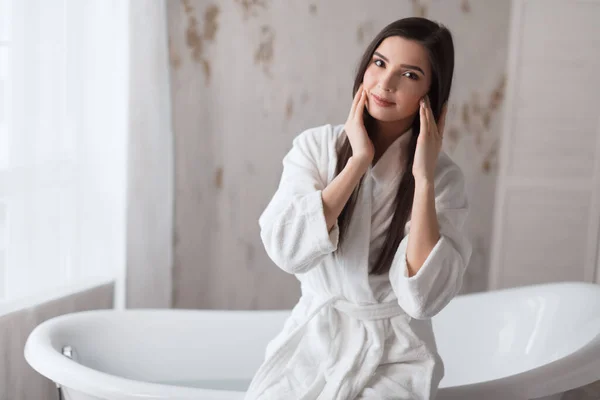 Brun-hårig kvinna i badrock, poserar med bara axlar bredvid badkaret — Stockfoto