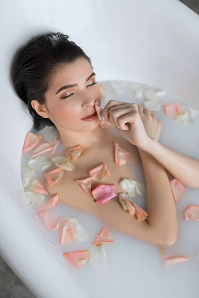 Mujer joven toma un baño de aroma de leche con pétalos de flores — Foto de Stock