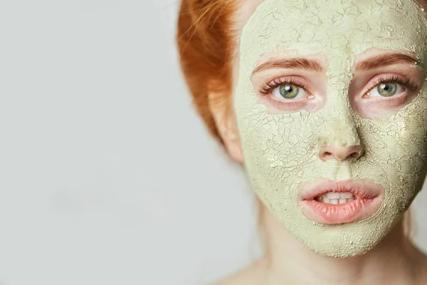 Ragazza dai capelli rossi emotivi con una maschera cosmetica di argilla verde sul viso — Foto Stock