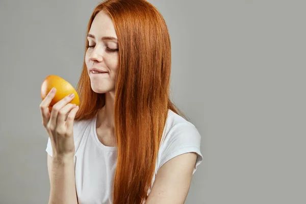 Agradable mujer de jengibre en camiseta blanca está probando la fruta —  Fotos de Stock