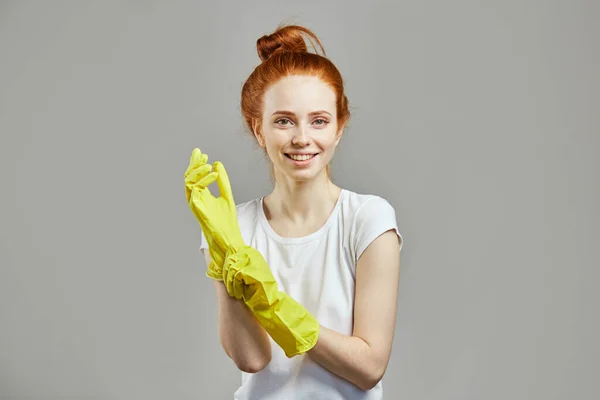 Joven mujer jengibre feliz poniendo en la mano guantes de goma amarillos. —  Fotos de Stock