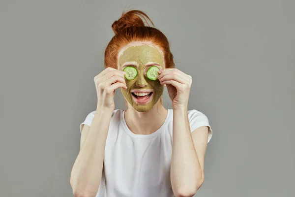 Hermosa joven alegre pelirroja mujer está recibiendo máscara de arcilla facial en el spa —  Fotos de Stock