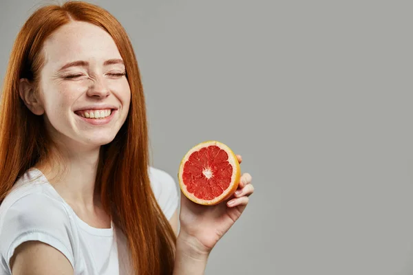 Lachend ehrfürchtig charmantes Mädchen mit geschlossenen Augen hält eine Hälfte Grapefruit — Stockfoto