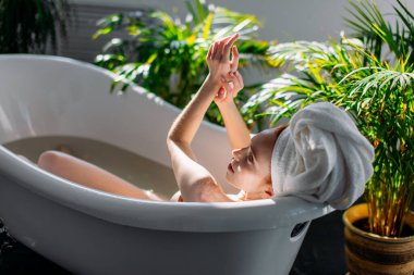 Kızıl saçlı kadın spa merkezinde köpükle küvette dinleniyor..