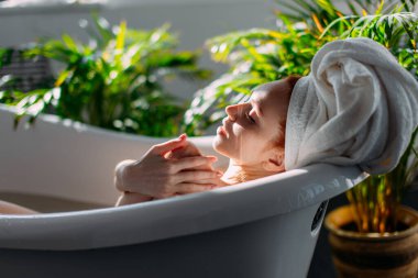 Kızıl saçlı kadın spa merkezinde köpükle küvette dinleniyor..