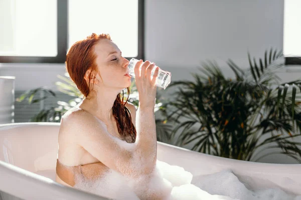 Mujer pelirroja relajándose en la bañera con espuma en el centro de spa. — Foto de Stock