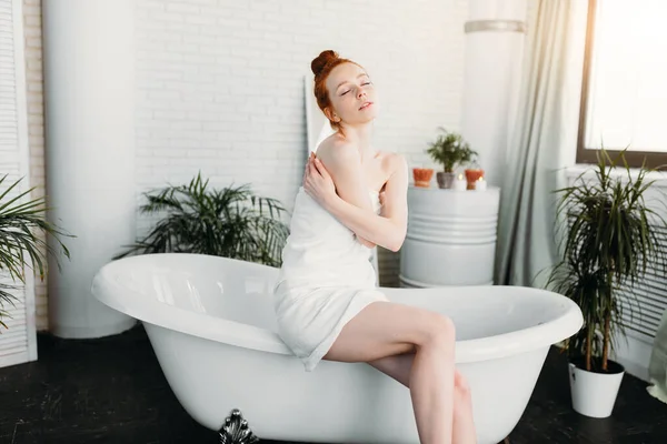 Pelirroja mujer preparando baño de espuma en amplio baño con plantas verdes — Foto de Stock