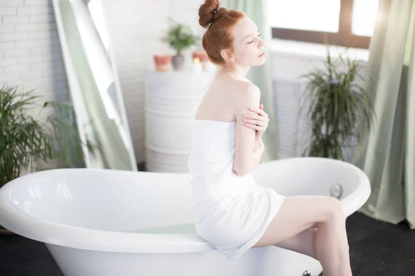 Pelirroja mujer preparando baño de espuma en amplio baño con plantas verdes — Foto de Stock