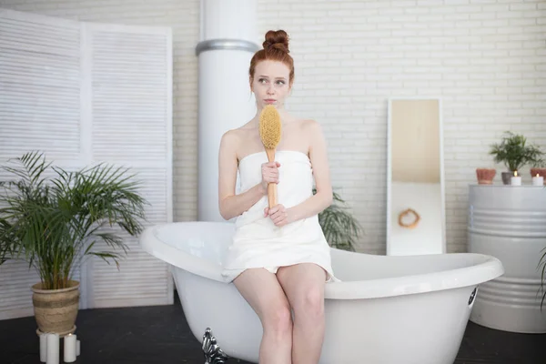 Femme rousse massant ses jambes avec une brosse pour le corps dans la salle de bain — Photo