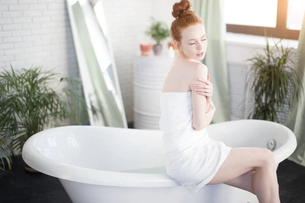 Femme rousse préparant bain en mousse dans une salle de bain spacieuse avec des plantes vertes — Photo