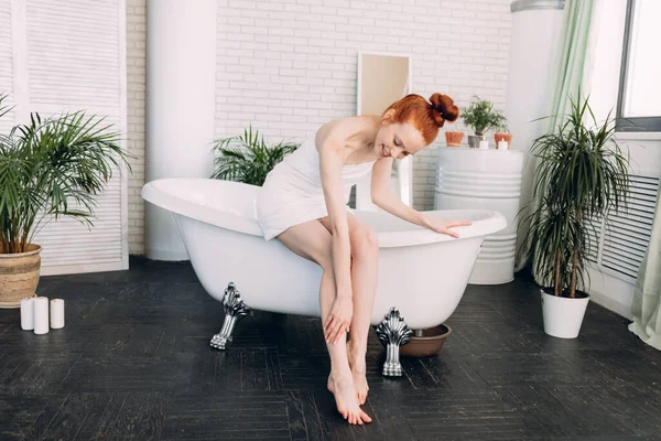 Mulher ruiva preparando banho de espuma em banheiro espaçoso com plantas verdes — Fotografia de Stock