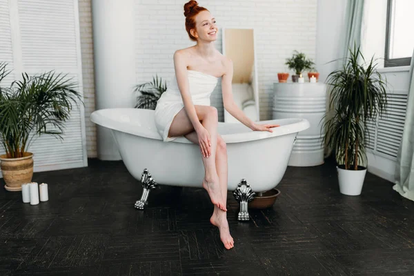 Pelirroja mujer preparando baño de espuma en amplio baño con plantas verdes —  Fotos de Stock