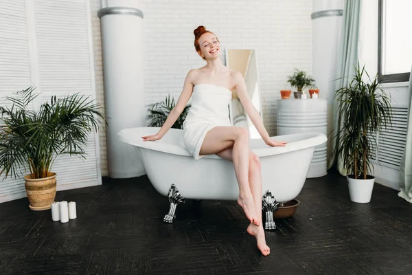 Femme rousse préparant bain en mousse dans une salle de bain spacieuse avec des plantes vertes — Photo