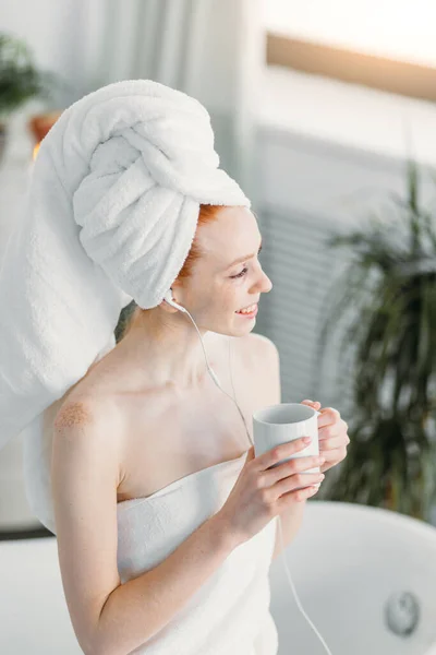 Šťastná žena v koupelně poslouchat hudbu a pít čaj sedí na vanu — Stock fotografie