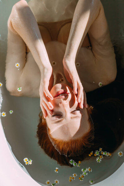 Чувственная женщина с длинными рыжими волосами расслабляется в воде с крошечными цветами
